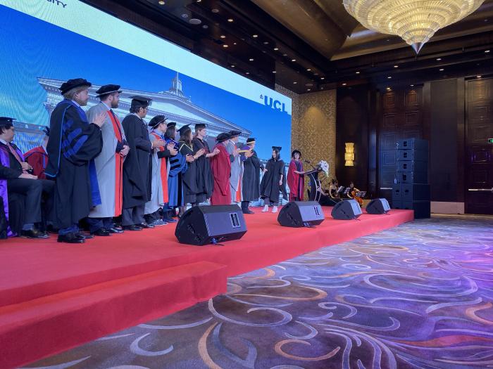 Stage with UCL School of Management academics in traditional dress greet the MBA graduates