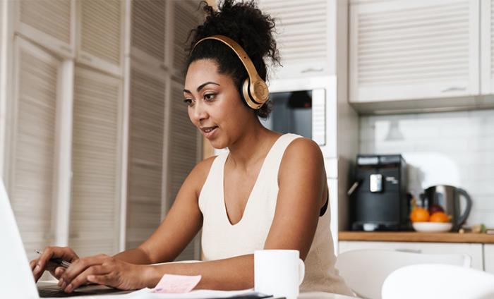 Woman working on a laptop wearing headphones in her kitchen