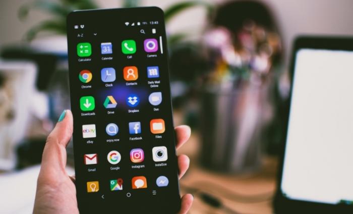 Photo of a hand holding a mobile phone with various apps on the display screen such as social media, email, notes.